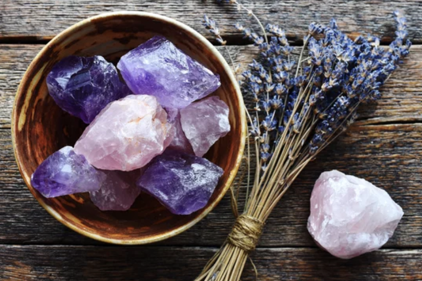 A bowl filled with amethyst crystals is placed alongside a bunch of freshly cut lavender and a rose quartz crystal, symbolizing the calming and healing energy of Reiki therapy.